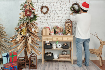 Man hanging handmade Christmas wreath on wall when decorating apartment for winter holidays