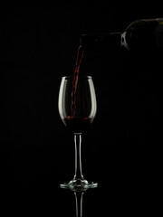 
wine and champagne glass on black background with pouring red wine