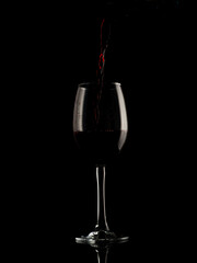 
wine and champagne glass on black background with pouring red wine