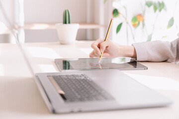 A hand holding a pencil and working with a laptop.