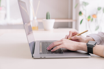 A hand holding a pencil and working with a laptop.