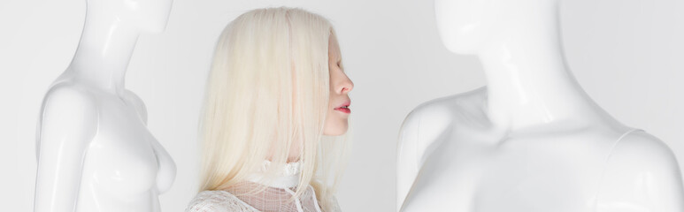 Side view of albino woman standing between mannequins isolated on white, banner.