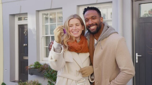Portrait of multi cultural couple outside house on moving day holding keys to new home in fall or winter - shot in slow motion