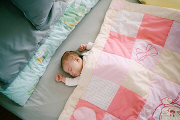 Infant sleeps on bed covered with pink patchwork quilt. Top view - obrazy, fototapety, plakaty