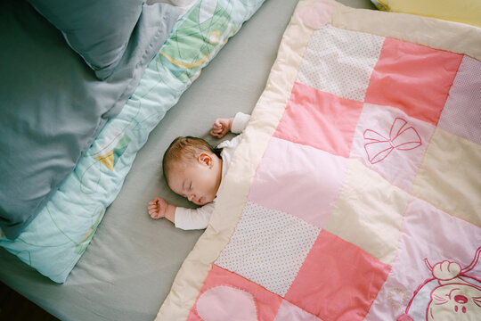 Infant sleeps on bed covered with pink patchwork quilt. Top view