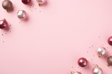 Top view photo of pink christmas tree decorations balls and gold sequins on isolated pastel pink background with copyspace