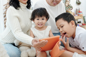 Adorable little girl, her bother and parents watching Christmas movie on tablet computer