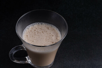 Latte iced coffee in a clear glass on a black background.