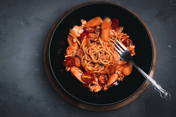 Spaghetti with tomato sauce, chicken and sausage in black plate top view. Flat lay.