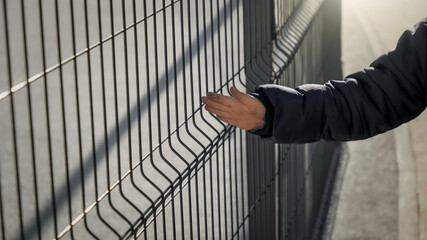 Closeup of boy touching metal net fence and walking past. Concept of poverty, immigration, bullying...