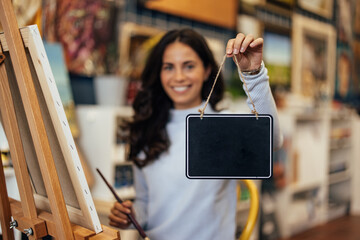 Portrait of a happy adult woman, holding a small blackboard by a thread.