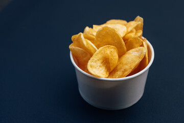 Picture of a paper cup full of salty chips, on a blue background.