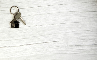 Silver key with silver house figure on white wooden background, buying new house real estate concept copy space