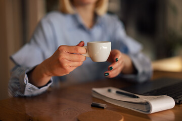 Closeup picture of a woman picking up a cup of coffee, during work.