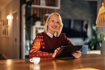 Portrait of smiling blonde woman, playing a video game on her tablet.