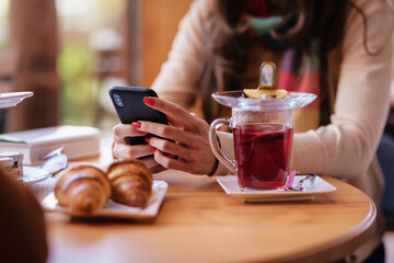 Close-up of woman's hand holding a mobile phone and text messaging while sitting in coffee shop