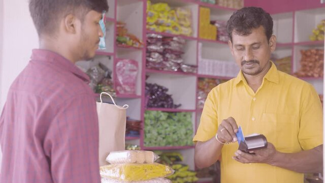 Indian customer making payment using credit card at groceries or Kirana shop - concept of digital or cashless payment, finance and Small business.
