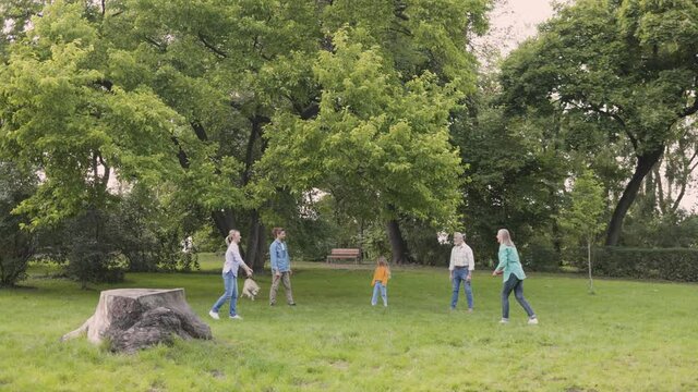 Weekend together. Full length view of the happy family playing at the frisbee at the park with their cute dog. People and leisure concept