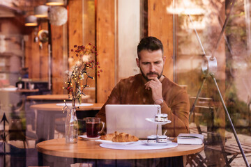 Thinking man using his laptop while sitting at desk in the cafe