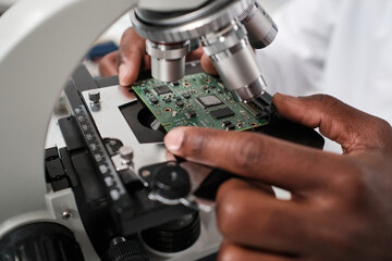 Part of hand of contemporary researcher putting circuit board in microscope before studying its characteristics