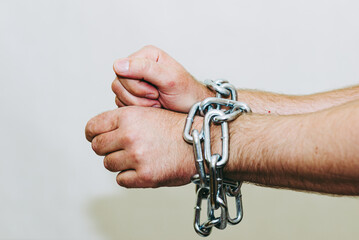 Men's hand in a steel chain.Steel chains in the hands of man on a gray wall...