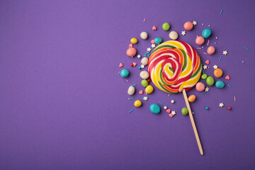 Colorful spiral lollipop with sprinkling on violet background. Vertical photo