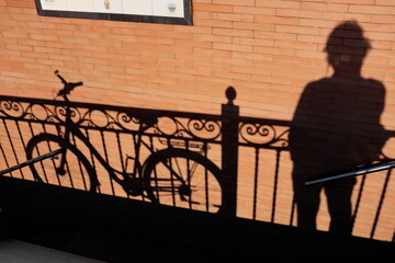 Ombres sur un mur ocre. Vélo et homme appuyés à une balustrade dans la rue. - obrazy, fototapety, plakaty