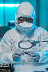 Young African man in protective gloves, eyeglasses and coveralls looking at microchip in magnifying...
