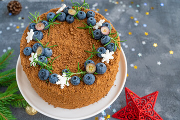 Chocolate honey cake decorated with fresh blueberries, rosemary and sugar snowflakes on top of a white stand. Cake for Christmas and New Year. selective focus