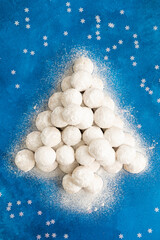 Christmas snowball cookies in powdered sugar decorated in the shape of a Christmas tree on a blue concrete background. Top view, copy space.