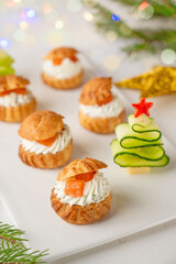 Festive savory profiteroles with salmon, cream cheese and dill on a white plate on a white background. Appetizer for Christmas and New Year. Selective focus.