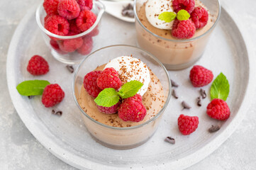 Chocolate mousse with whipped cream and fresh raspberries in a glass on a gray concrete background. Copy space.