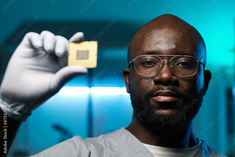 Poster young serious man of african ethnicity holding microchip in gloved hand while standing in front of c
