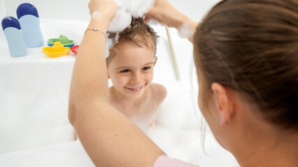 Funny shot of mother playing with her son in bath and making him stylish haircut