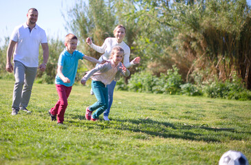 Fototapeta premium Father with mother with two children enjoy playing soccer on lawn in summer park