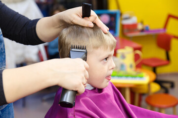 Children's hairdresser. The haircut of a little boy with fair skin.