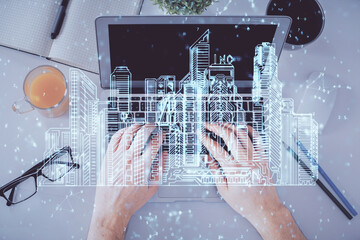 Double exposure of man's hands typing over computer keyboard and buildings drawing. Top view. smart city concept.