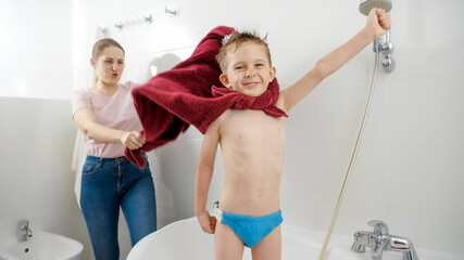 Funny shot of happy smiling boy with mother playing in bathroom and pretending to be comics hero