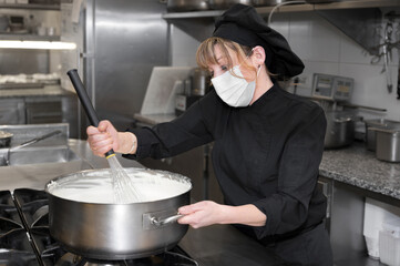 Health protection, safety and pandemic concept - Female chef cook wearing a protective face mask while working at restaurant kitchen. High quality photo