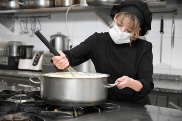 Health protection, safety and pandemic concept - Female chef cook wearing a protective face mask while working at restaurant kitchen. High quality photo
