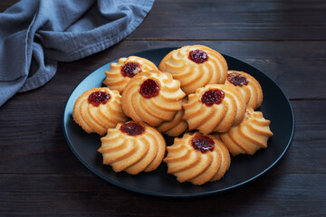 Kurabye shortbread cookies with berry jam in a black plate. Delicious dessert, dark wooden background.