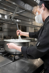 Health protection, safety and pandemic concept - Female chef cook wearing a protective face mask while working at restaurant kitchen. High quality photo