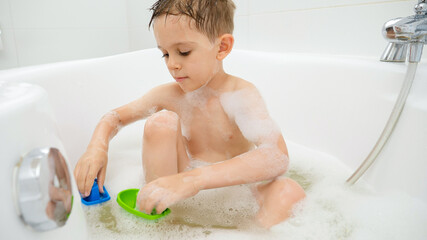 Cute boy washing in bath and having with plastic toys. Concept of family time, children development...