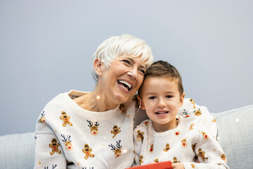 Beautiful family portrait. Happy little boy embracing his grandmother sitting on lap celebrating holidays together. Christmas tree on background. Family Christmas concept.