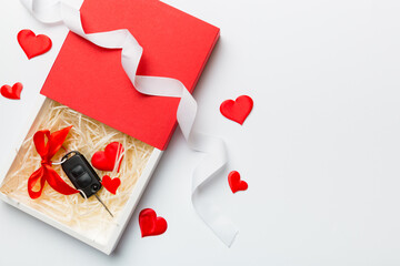 Black car key in a present box with a ribbon and red heart on colored background. Valentine day...