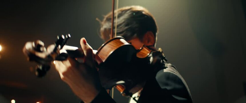 CU HANDHELD Portrait of young aspiring musician playing violin on a stage of a large venue. Shot with 2x anamorphic lens