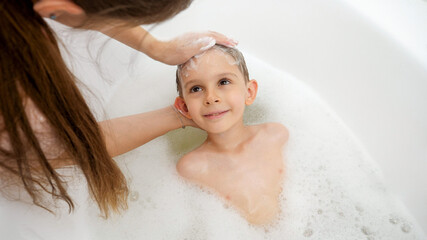 Obraz premium Portrait of smiling boy lying in bath while mother washes his head and hair with shampoo