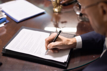 Hand of contemporary lawyer or businessman signing contract or other juridical paper while sitting by table