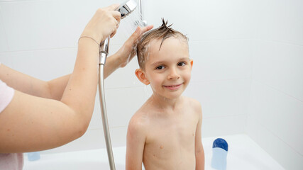 Young smiing boy looking in camera while mother washing his head in shower