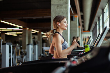 Fototapeta na wymiar Young fit woman jogging on a treadmill in modern gym. Cardio workout